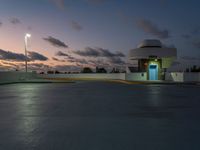 a large building at dusk in an empty parking lot near a street light and parking lot