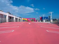 an empty red parking lot with blue skies in the background behind it is a multi - colored parking garage