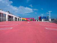 an empty red parking lot with blue skies in the background behind it is a multi - colored parking garage