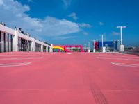 an empty red parking lot with blue skies in the background behind it is a multi - colored parking garage