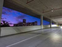 a parking lot has an empty concrete space with cars parked on the side and the sky at dusk