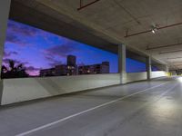 a parking lot has an empty concrete space with cars parked on the side and the sky at dusk