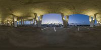 a plane is parked under a massive arch with concrete beams and concrete posts, while the sun goes down