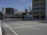 an empty parking lot with city buildings in the background and a car parked on the sidewalk