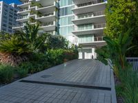 the entrance to an apartment with palms trees and bushes in the foreground, next to a concrete driveway