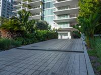 the entrance to an apartment with palms trees and bushes in the foreground, next to a concrete driveway