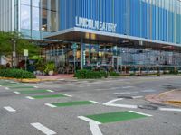 an outside city mall with green and white lines, a large glass front building, and some trees