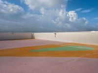 tennis court with green and orange markings on it's surface, under the cloudy sky