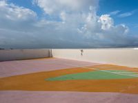 tennis court with green and orange markings on it's surface, under the cloudy sky