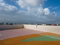 tennis court with green and orange markings on it's surface, under the cloudy sky