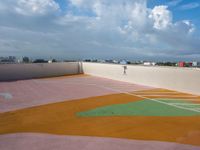 tennis court with green and orange markings on it's surface, under the cloudy sky