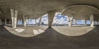 an outdoor skate park with concrete and circular mirrors, under blue sky and clouds with buildings and trees