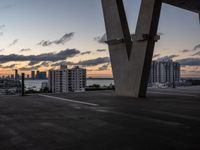 the sun sets over a view of some buildings in a city across the water from a tall structure