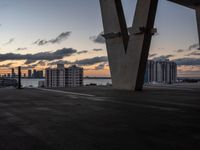 the sun sets over a view of some buildings in a city across the water from a tall structure