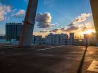 a tall concrete bridge over a cityscape at sunset with the sun setting through some clouds