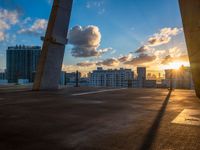 a tall concrete bridge over a cityscape at sunset with the sun setting through some clouds