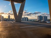 the sunset shines behind a large bridge as a car drives underneath it on a road beside large city buildings