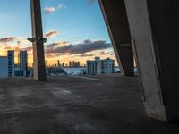 a tall building sitting under a large bridge in front of the sunset in a large city