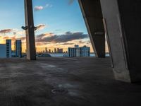 a tall building sitting under a large bridge in front of the sunset in a large city