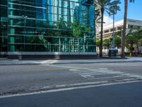 the street sign is at the end of the empty road where the tall buildings are reflected in the glass of the building