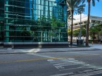 the street sign is at the end of the empty road where the tall buildings are reflected in the glass of the building