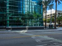 the street sign is at the end of the empty road where the tall buildings are reflected in the glass of the building