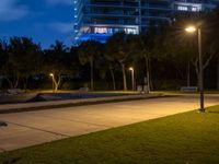 two benches sitting on the grass at night, next to an empty parking lot and tall buildings