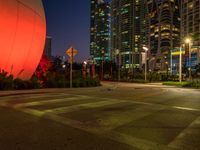 a photo of a large orange balloon and other lights on buildings in a city at night