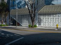 a yellow fire hydrant sitting next to a street under a building with lattices