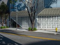 a yellow fire hydrant sitting next to a street under a building with lattices