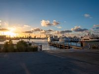 there are many boats docked at the pier in this photo the sun sets over the city