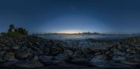 the sun rises behind the manhattan skyline as seen from the rocks by the water's edge