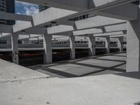 a train station with cars parked under a bridge and white structure overpassing it