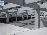 a train station with cars parked under a bridge and white structure overpassing it