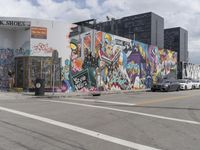 graffiti art on the side of a building near cars parked in front of it and people standing in a parking area