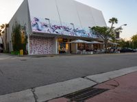 a large white building covered in graffiti sits on a street corner next to a tree line