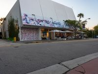 a large white building covered in graffiti sits on a street corner next to a tree line