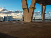 a parking lot with cars parked under an overpass and tall buildings in the distance