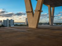 a parking lot with cars parked under an overpass and tall buildings in the distance