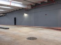 a parking lot inside of an empty building with cement flooring and pipes hanging from the ceiling