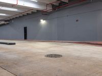 a parking lot inside of an empty building with cement flooring and pipes hanging from the ceiling