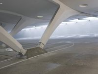 a man rides a skateboard while leaning against a wall in a parking garage under a slant roof