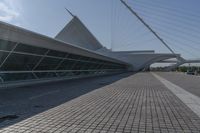 a very long curved glass building next to a river bed area with cars passing by