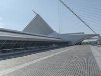 a very long curved glass building next to a river bed area with cars passing by