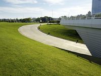 a long curved road on the grass in front of a building with people walking on it