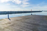 the dock is empty of people sitting on the ledge looking out at the water and a sailboat