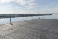 the dock is empty of people sitting on the ledge looking out at the water and a sailboat