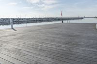 the dock is empty of people sitting on the ledge looking out at the water and a sailboat