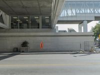 the empty street has an orange traffic sign near a concrete building with windows and a high rise above it