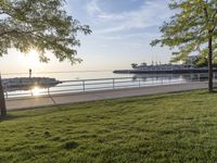 an empty park with grassy area and benches in it and a dock behind the trees